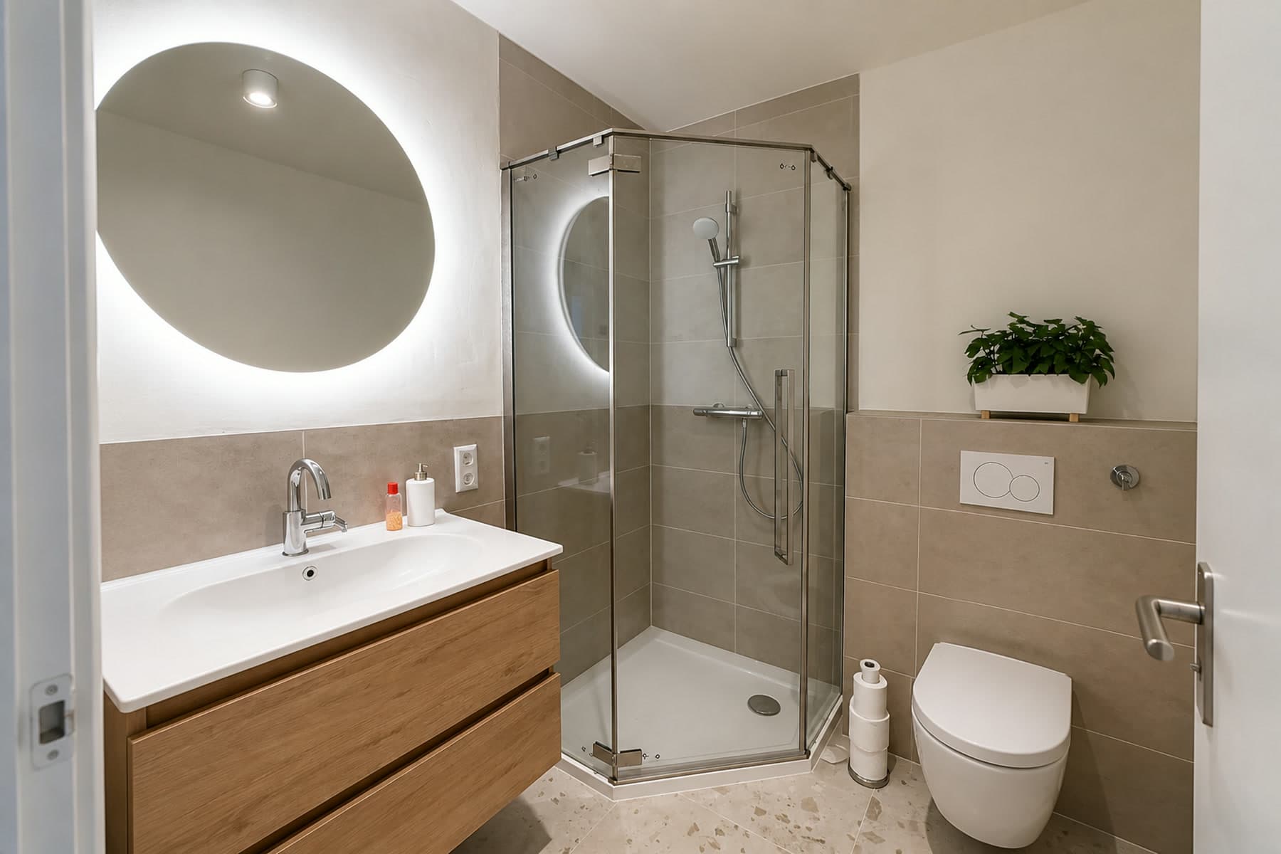 Dezelfde badkamer na renovatie, met houten wastafelmeubel, verlichte ronde spiegel en nieuwe douchecabine