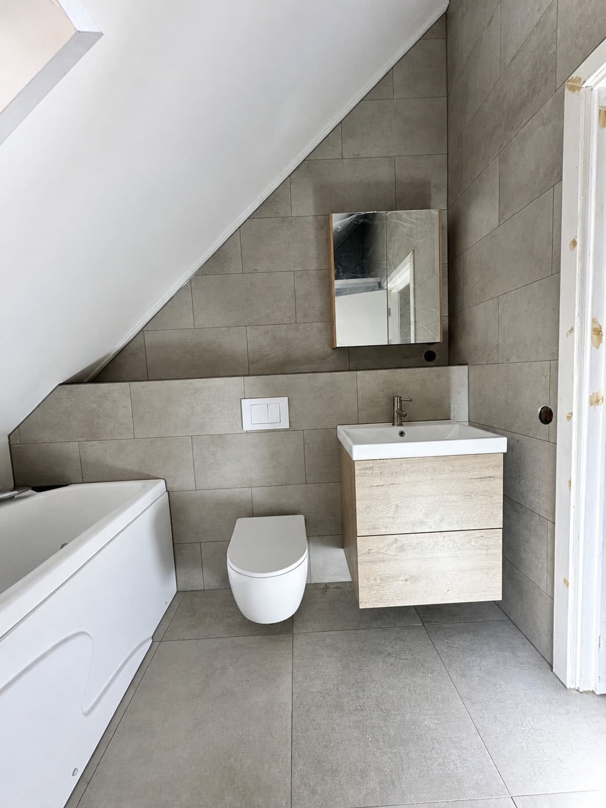 Afgewerkte badkamer met bad, wandcloset en wastafelmeubel onder het schuine dak