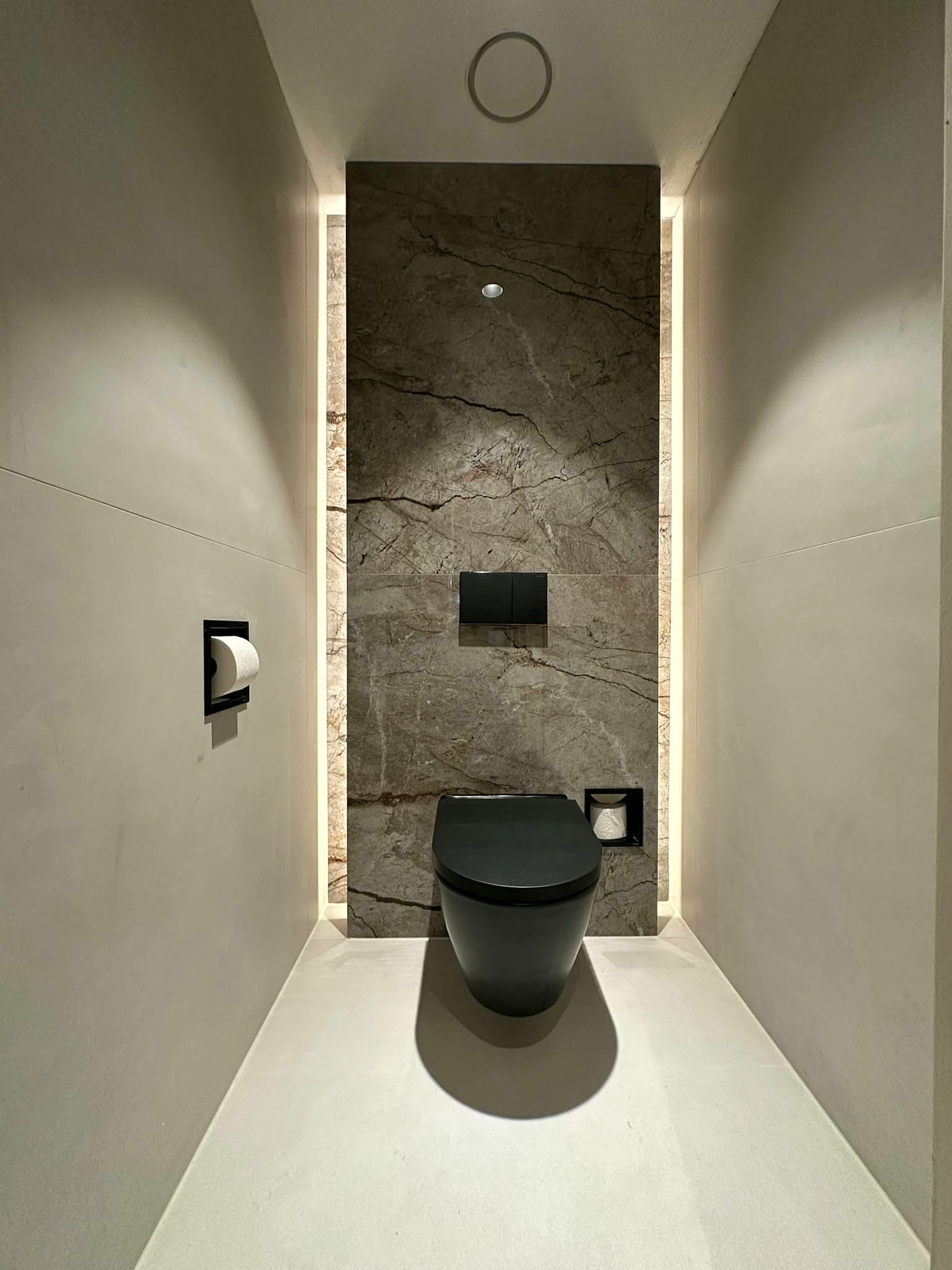 Wandtoilet met donkere afwerking en verlichte natuursteenwand