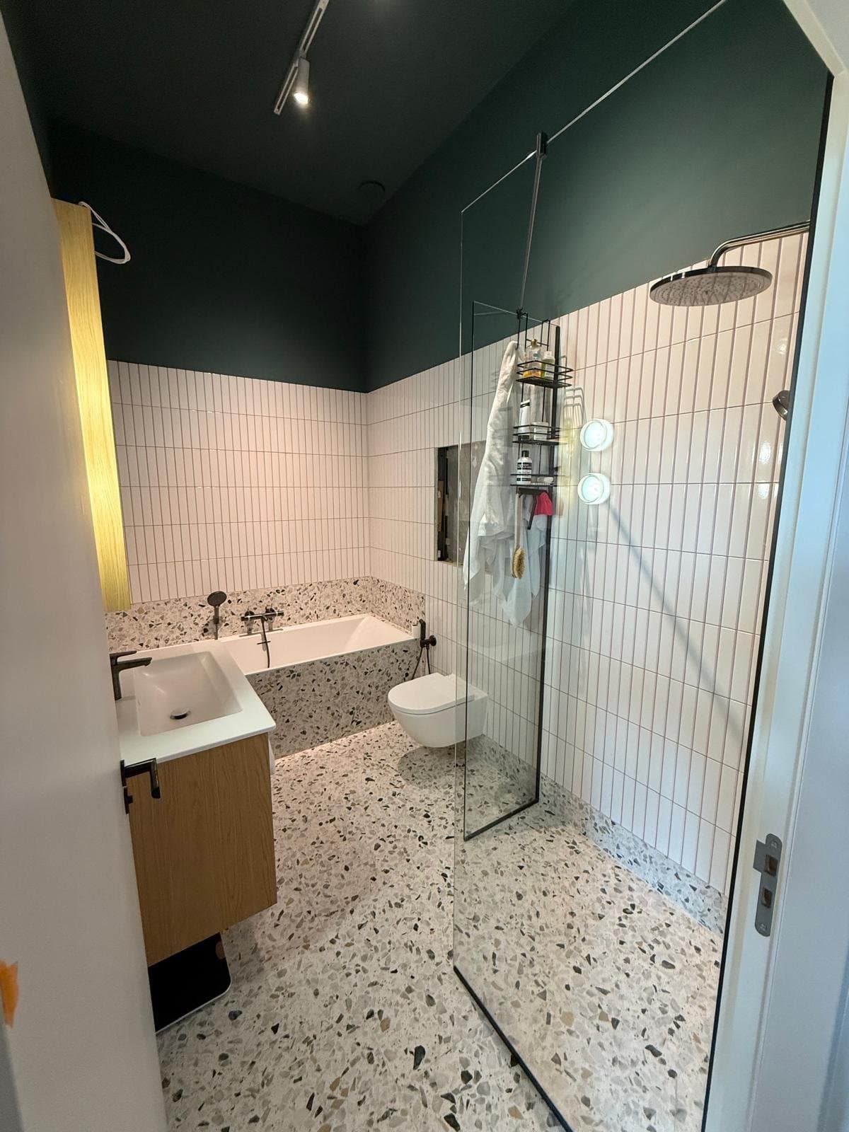 Badkamer met terrazzovloer, witte staaftegels, donkergroene wand, bad en inloopdouche